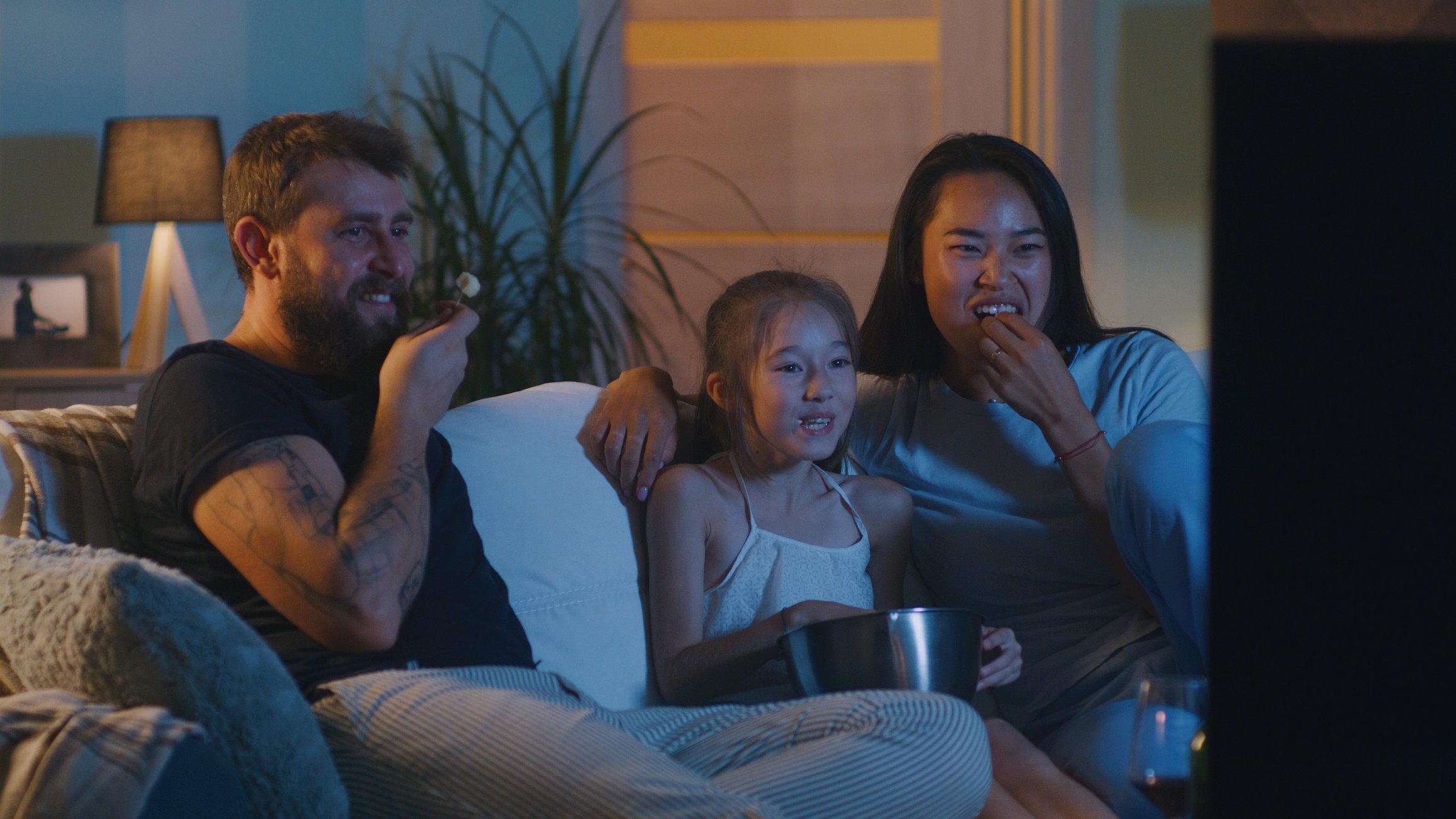 A family of three sitting on the couch watching television.
