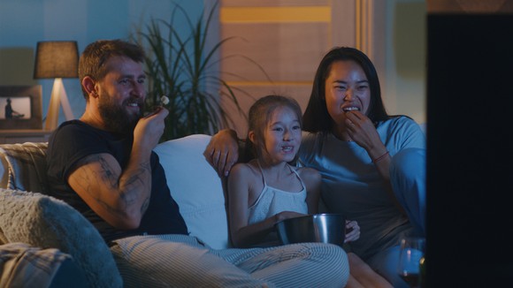 A family of three sitting on the couch watching television.