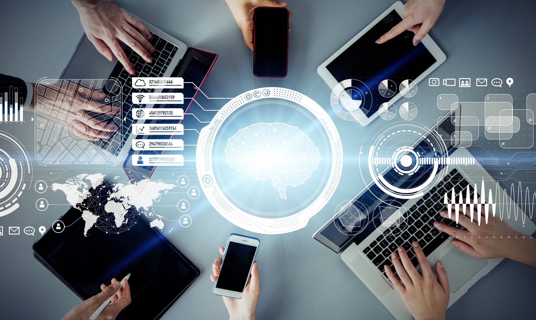 An overhead view of many connected devices on a table with people's hands using them.
