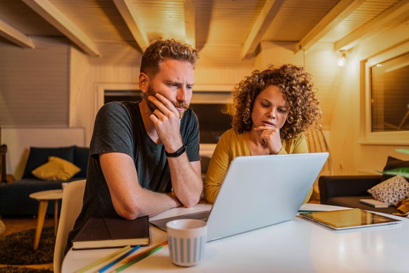 Two people with concerned facial expressions looking at a laptop.