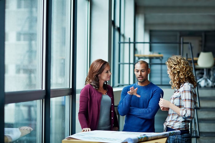 Three colleagues discussing an issue in-office over a table.