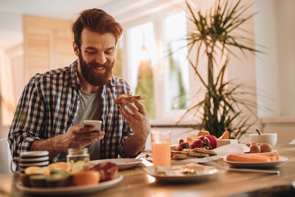 Smiling person checking their phone while eating toast.