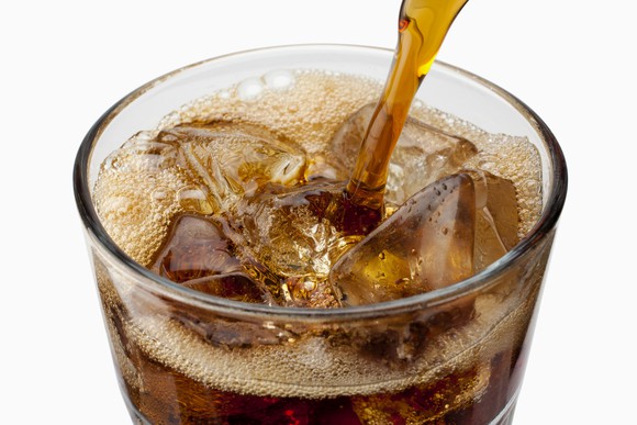 Cola being poured into a glass with ice.