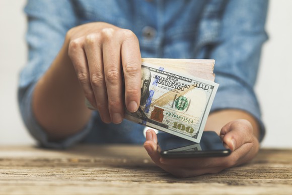 Person holding cash and a mobile phone in their hands.