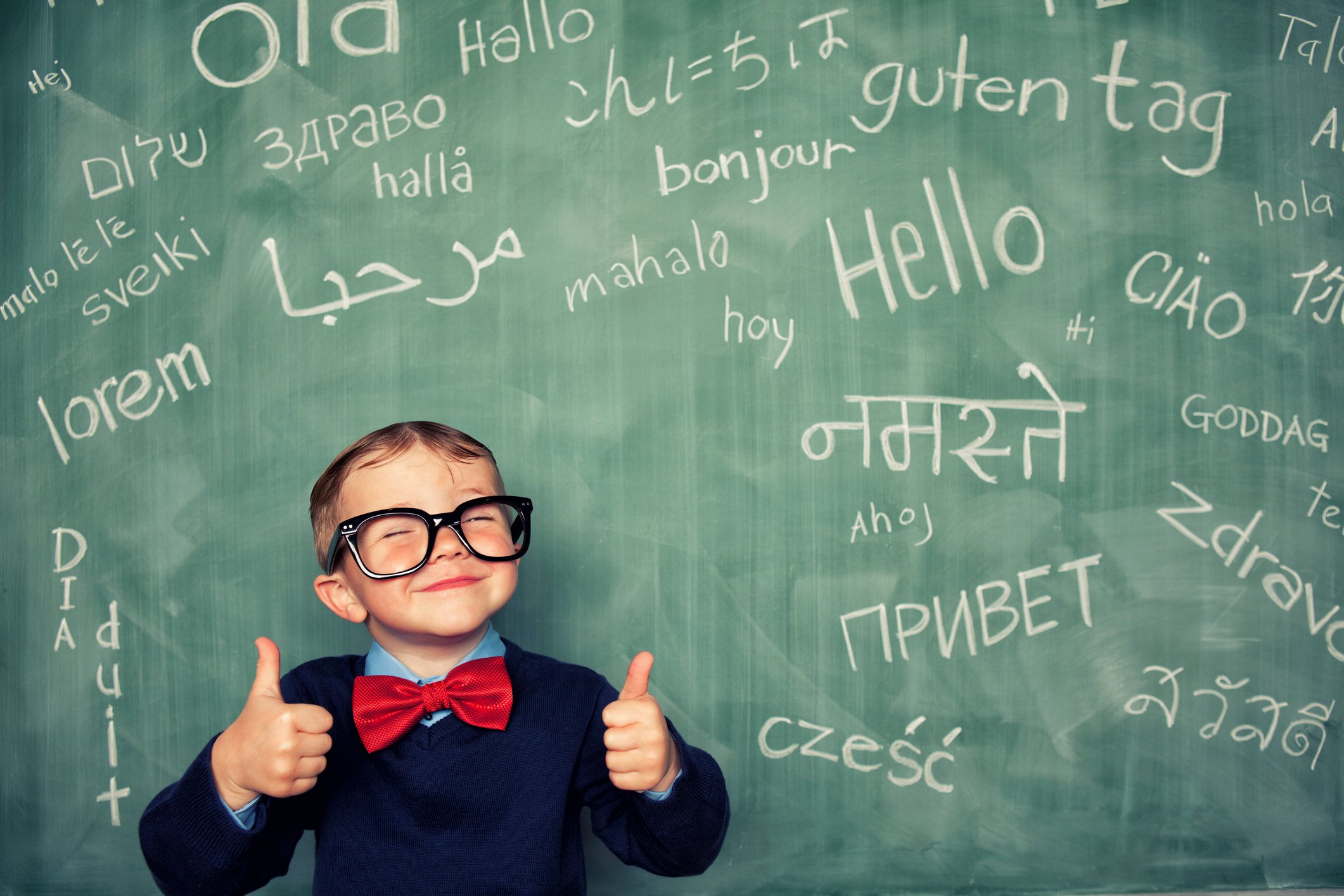 A young student stands in front a blackboard that shows hello in many languages. 