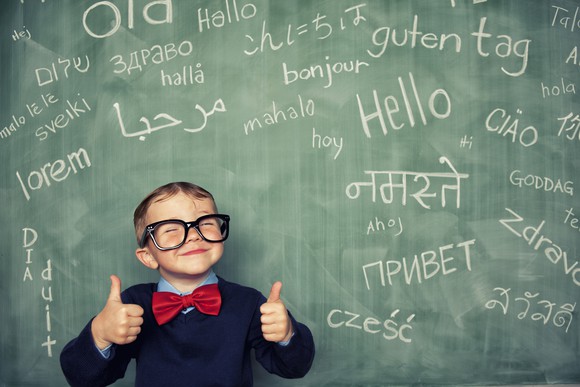 A young student stands in front a blackboard that shows hello in many languages. 