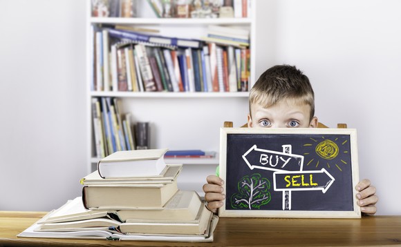 A child holds a blackboard with "buy" and "sell" arrow signs.