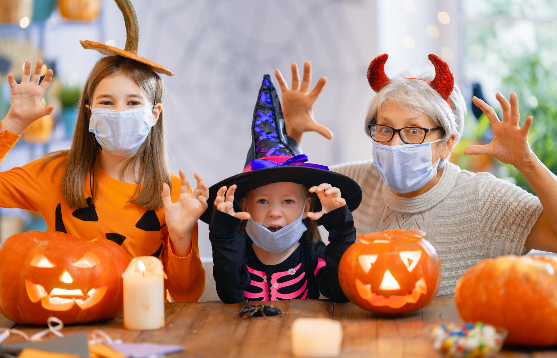 An older person and two children dress up for halloween and raise their arms in a scary manner at the camera.