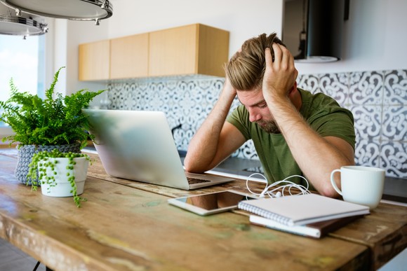 A person holding their head, looking at a laptop.