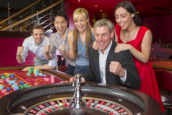 A group of happy, excited gamblers watching a roulette wheel.