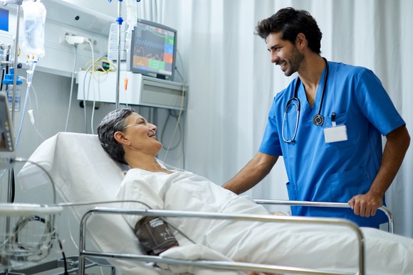 A patient in a hospital bed with a healthcare professional at the bedside.