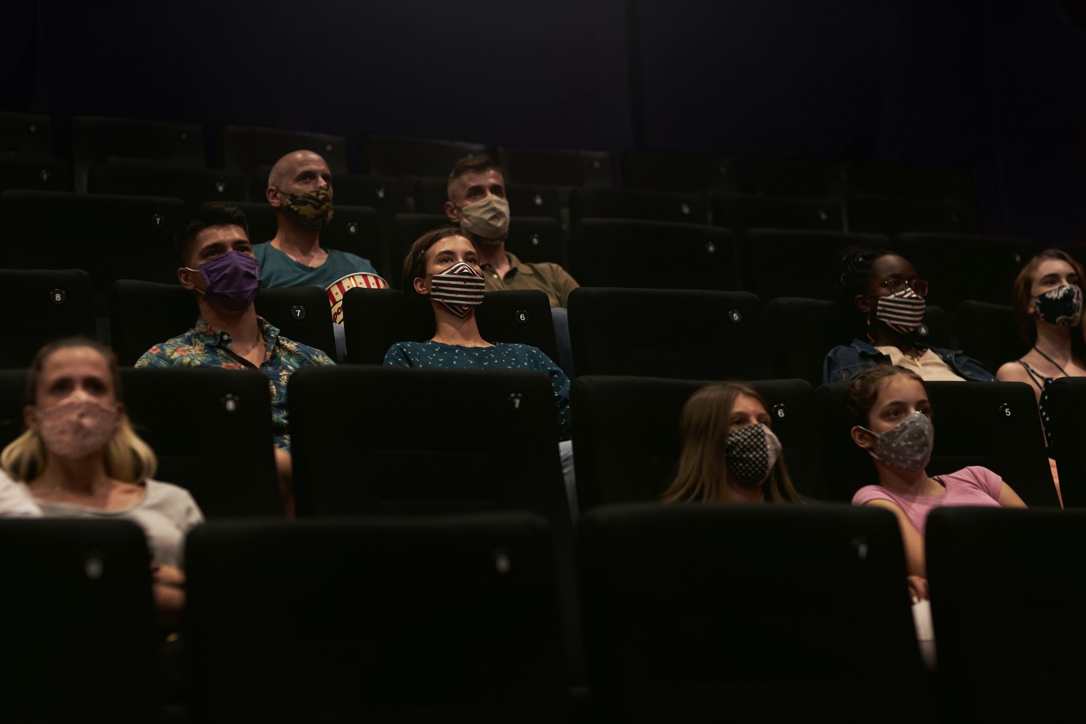 A few people scattered in a movie theater wearing masks.