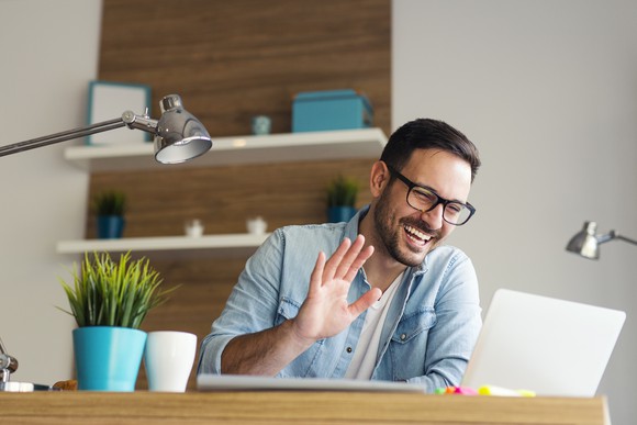 A person waving at a computer screen.