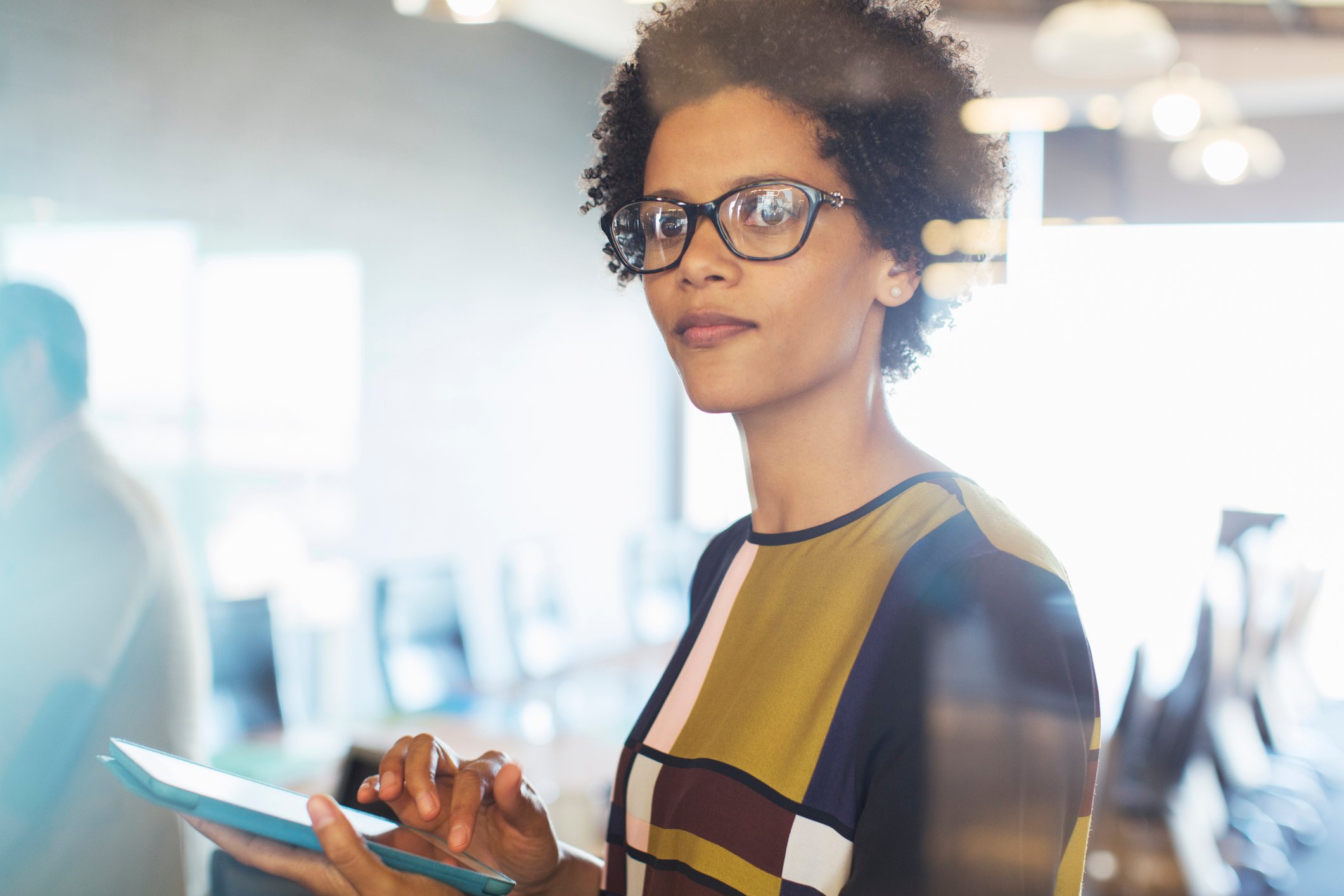 A business woman in her office, looking up from her tablet. 