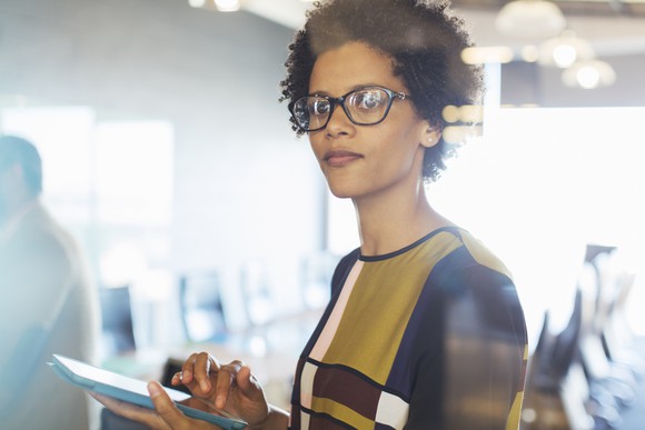 A business woman in her office, looking up from her tablet. 
