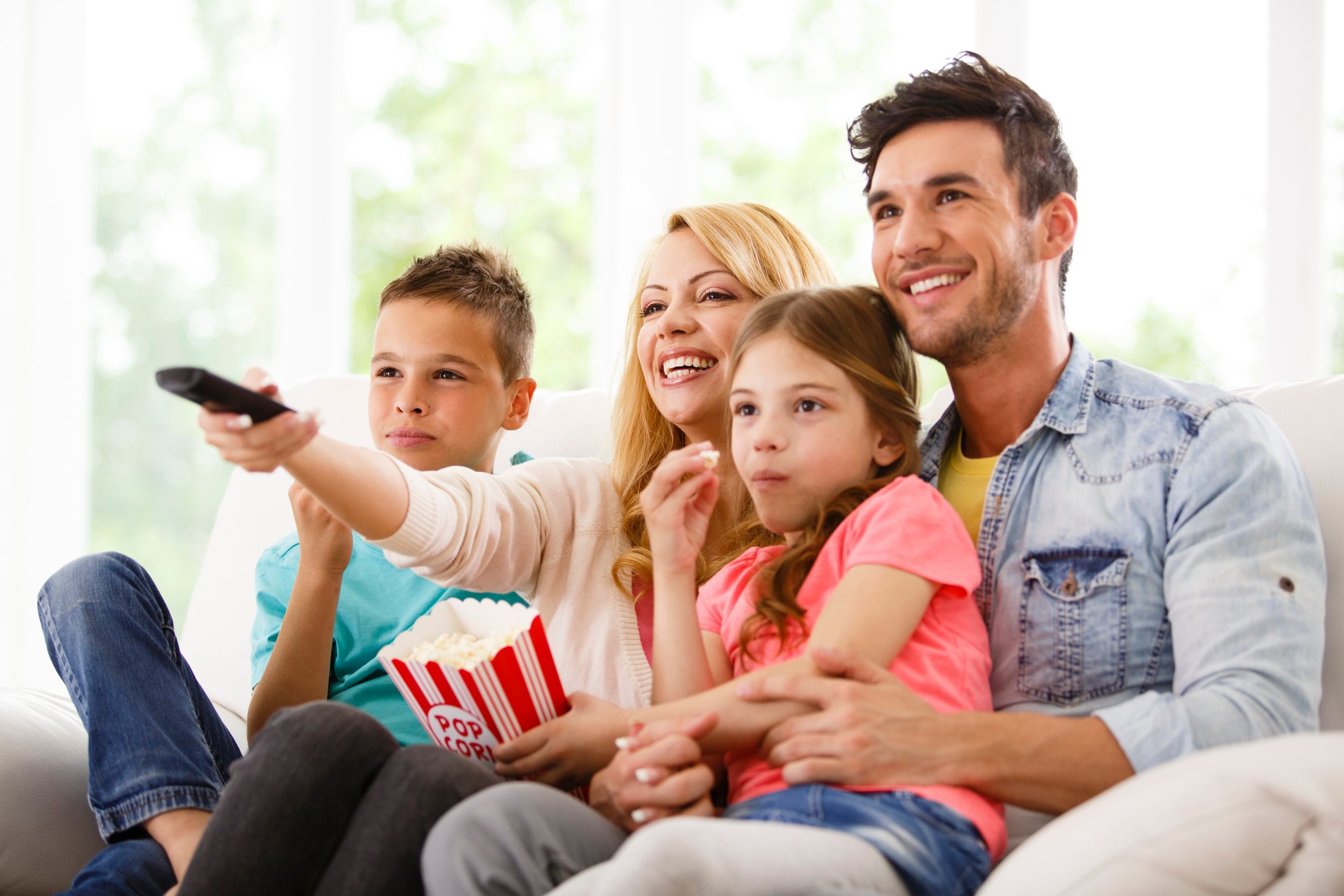 A family of four sitting on a couch, eating popcorn, and watching TV.
