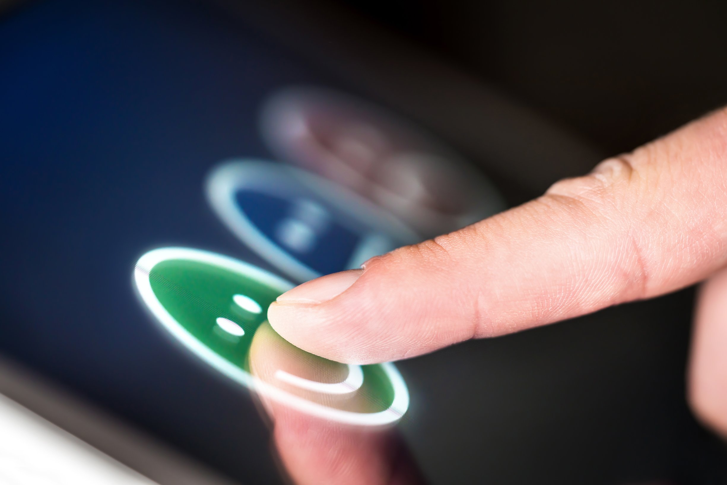 Finger pressing on a happy face among three different emoji on a tablet screen.