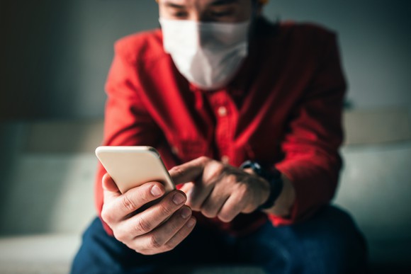 A person wearing a face mask touches the screen of their phone.