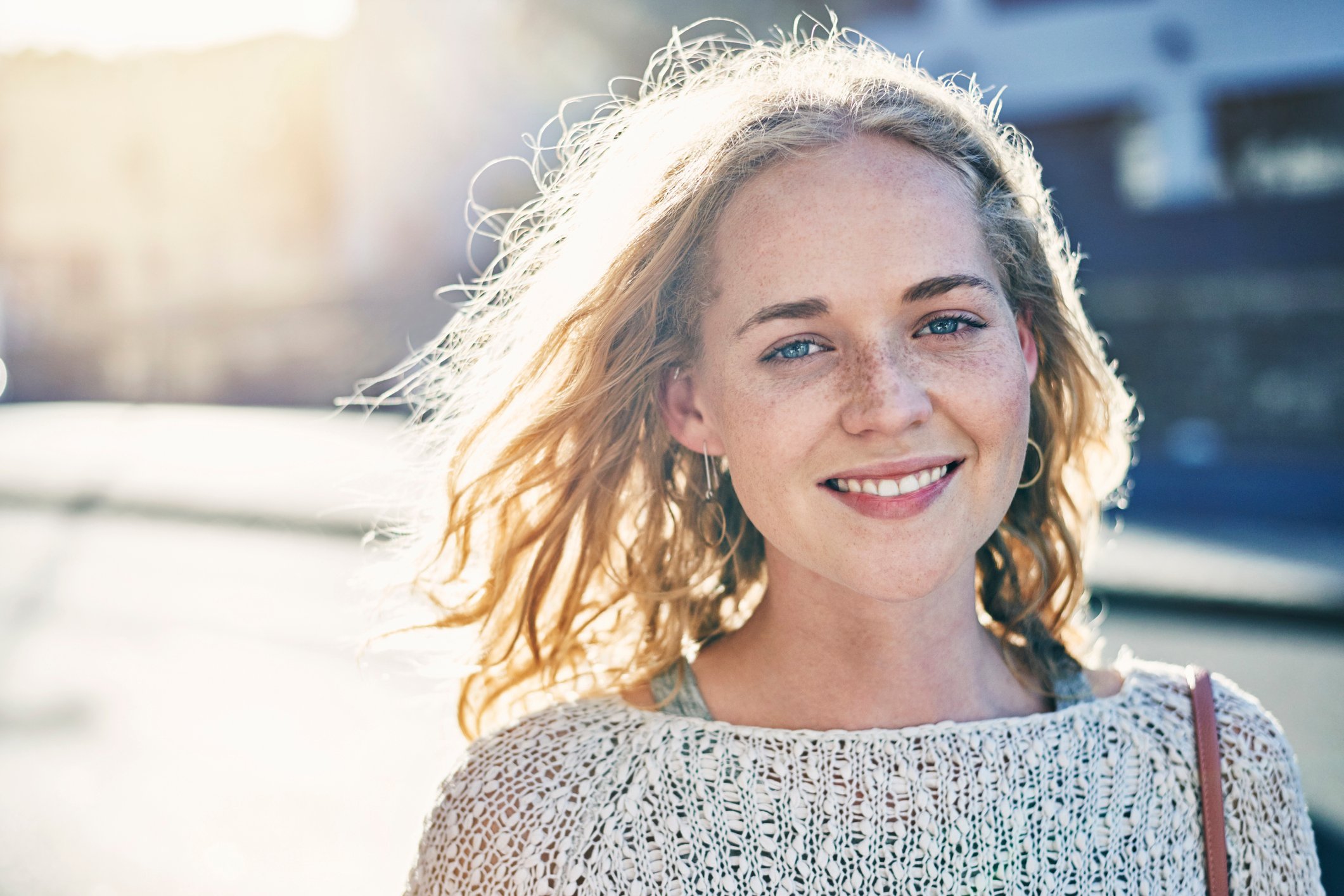 happy young woman smiling into camera against sunlit background