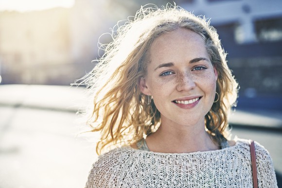 happy young woman smiling into camera against sunlit background