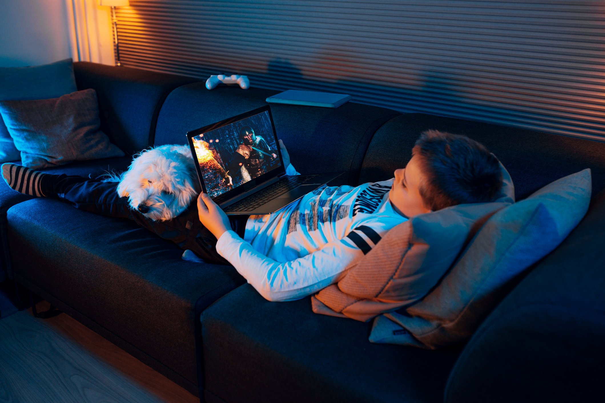 Child watches video on laptop while lying on sofa.