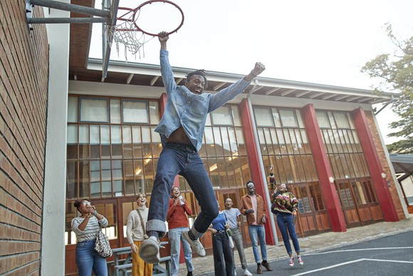 Person wearing jeans hanging from basketball hoop.