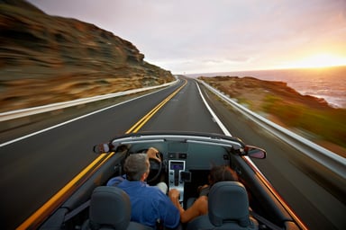 A couple drive in a convertible at sunrise.