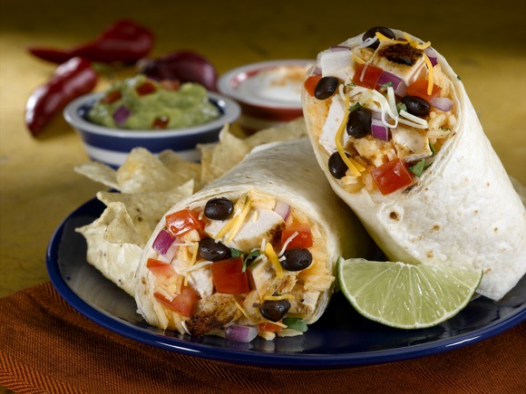 A burrito, chips, and a lime on a plate.