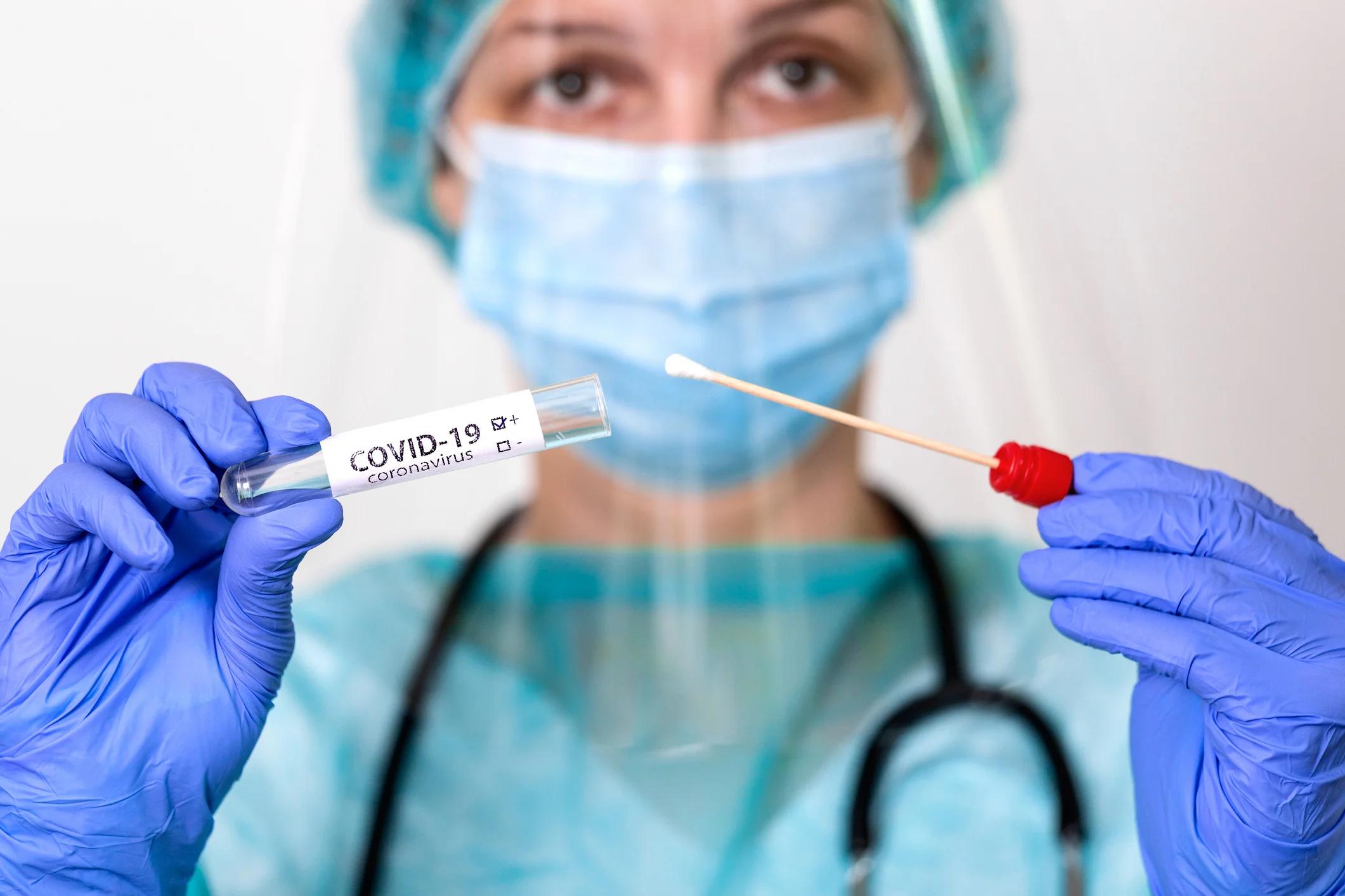 Medical professional holding swab and test tube marked COVID-19.