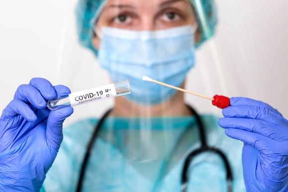 Medical professional holding swab and test tube marked COVID-19.