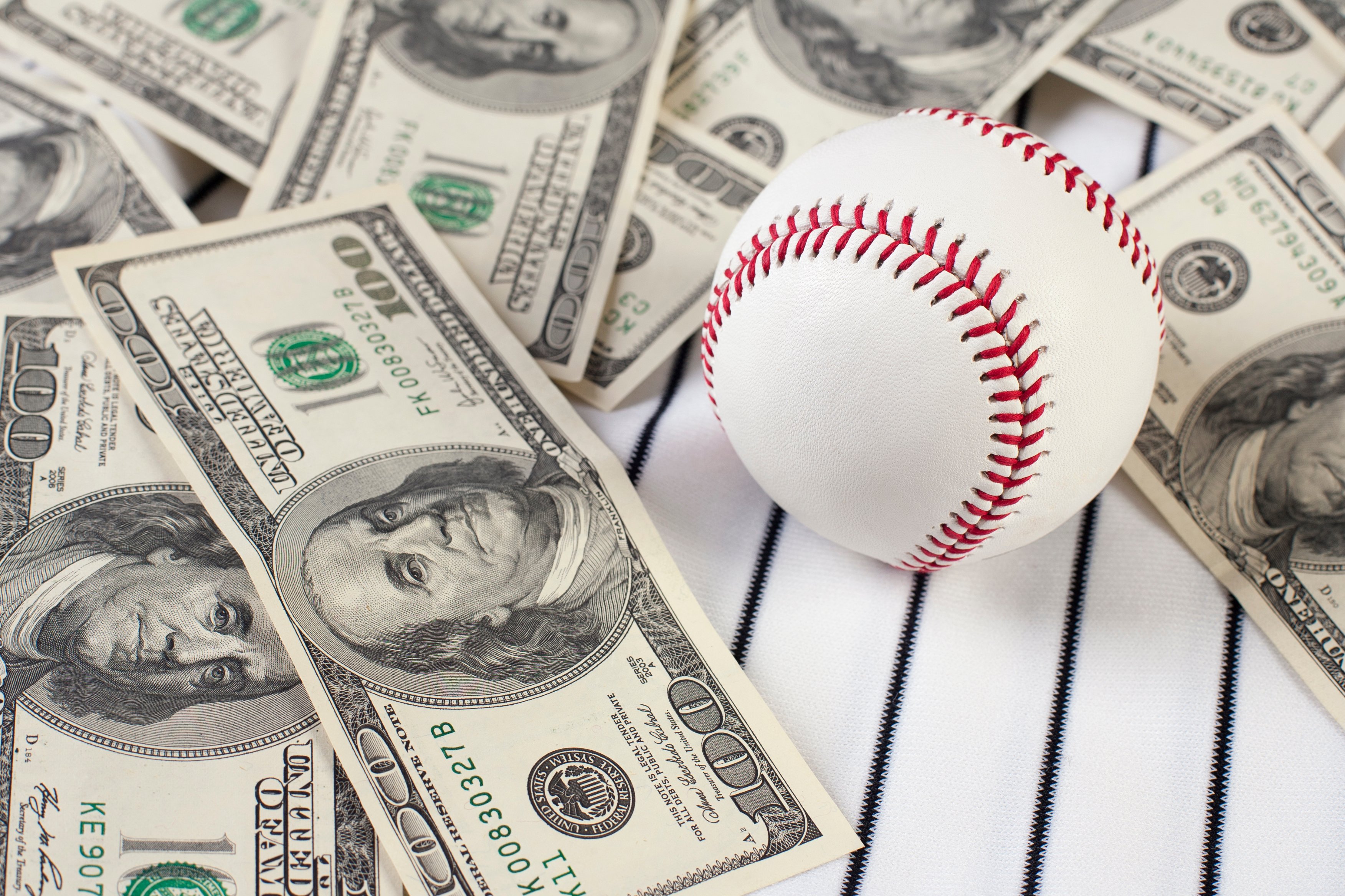 A baseball sits on a table with several $100 bills.