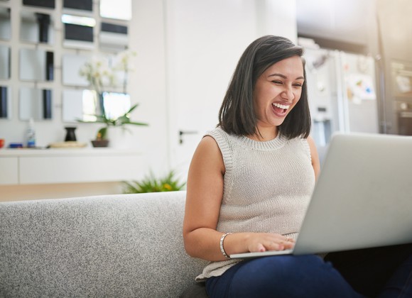 A smiling person looking at a laptop.