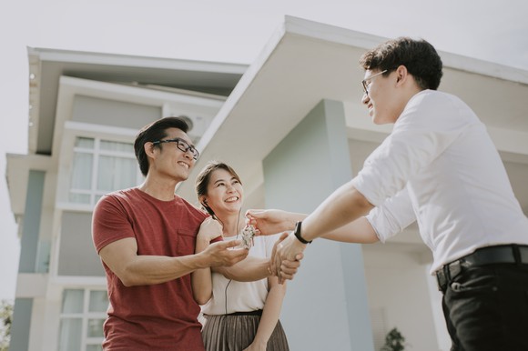 A smiling person handing a smiling couple the keys to a house.