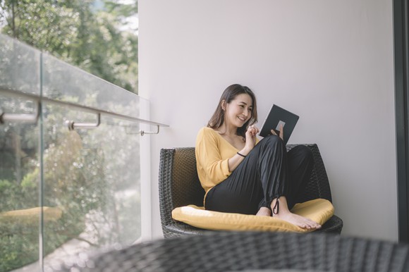 A person uses a tablet computer while sitting next to a window.