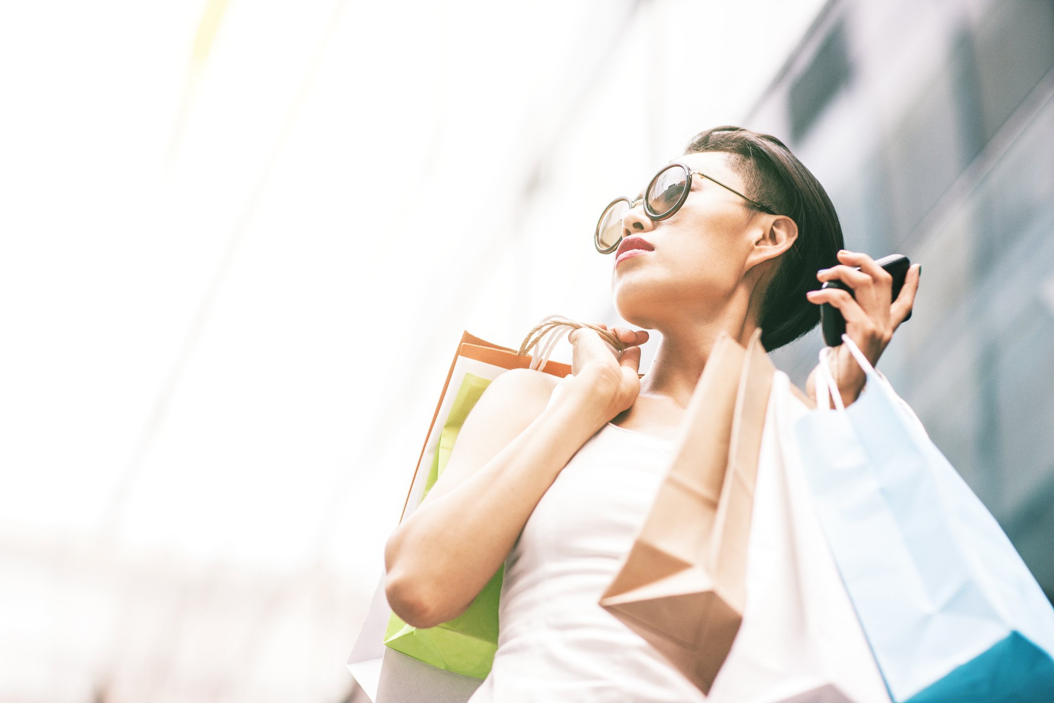 A stylish person wearing sunglasses and holding a cell phone and an armload of shopping bags.