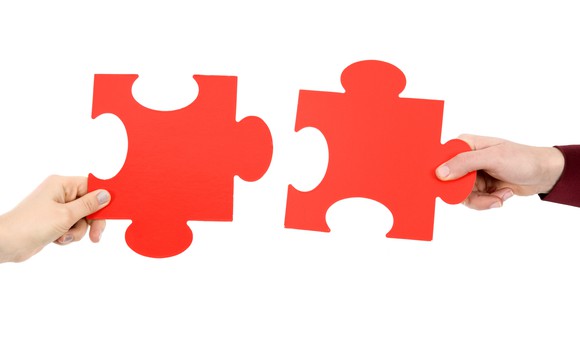 Two hands putting two red puzzle pieces together.