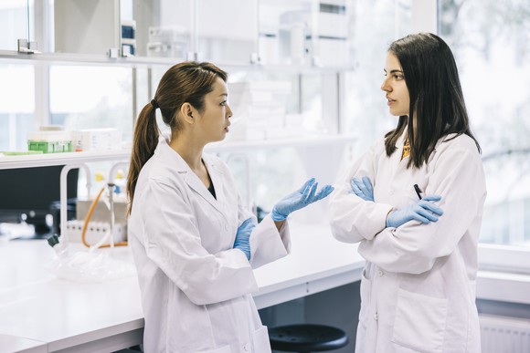 Two scientists talk while standing in their laboratory bay.