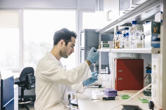 A scientist uses a pipette to transfer some fluid as he works at a laboratory bench.