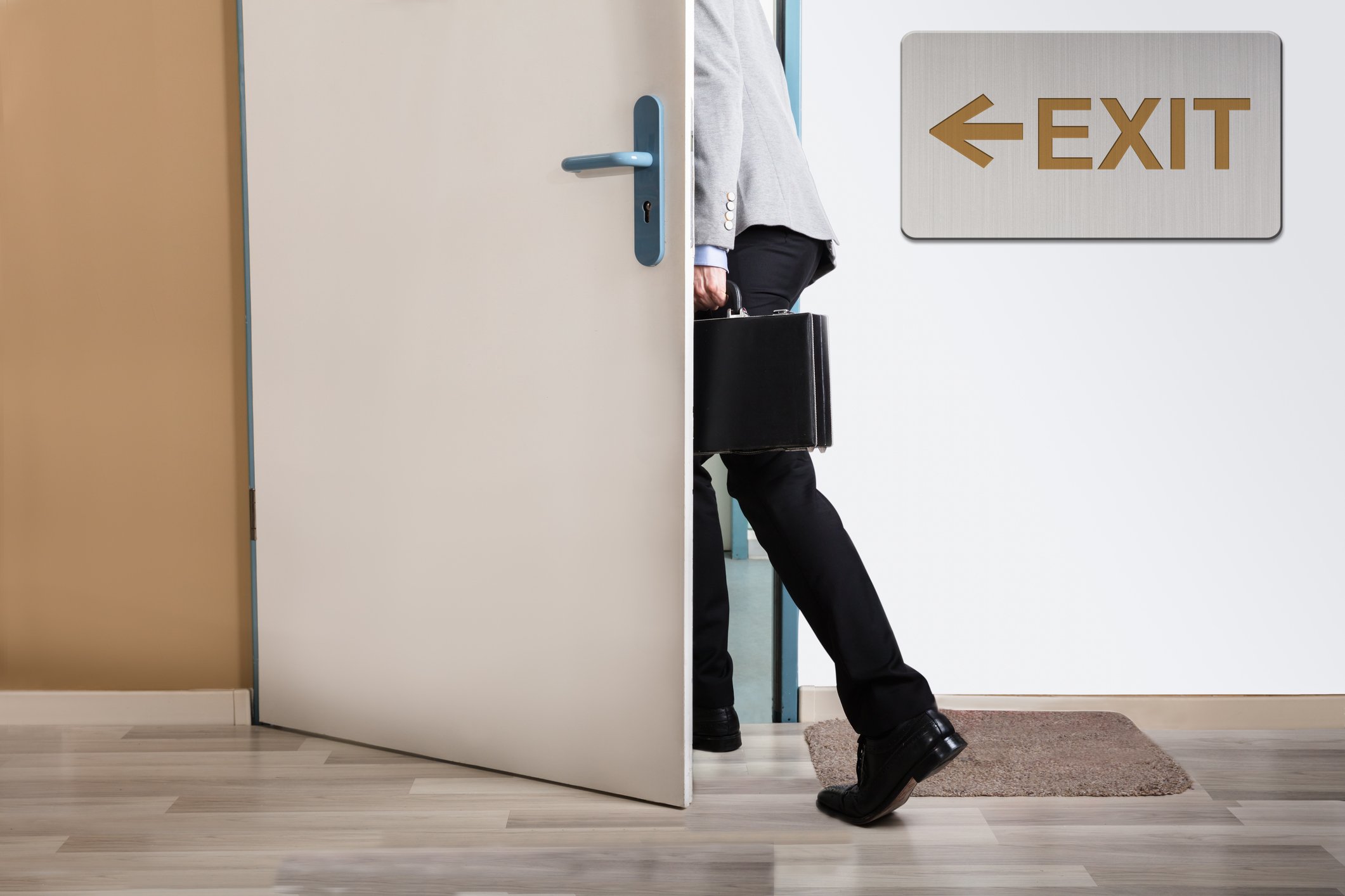 A person holding a briefcase walking through a doorway next to an exit sign.