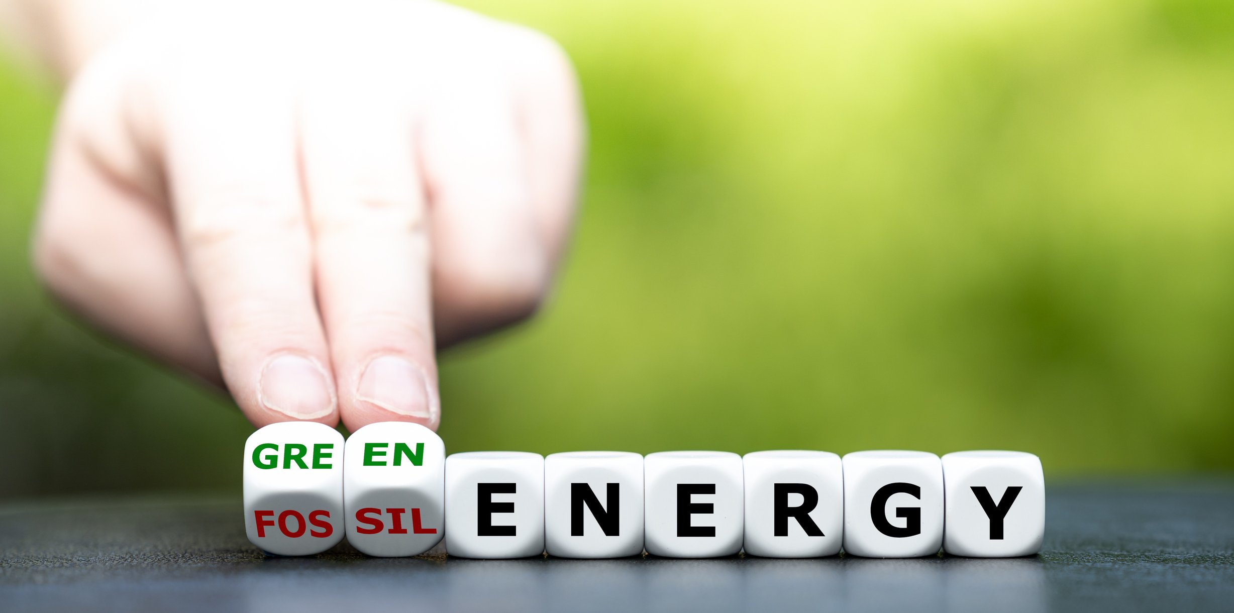 Dice with letters that spell out the word "energy." Two dice are being flipped from saying "fossil" to "green."