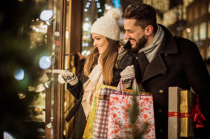 Two people with shopping bags looking through a store window.