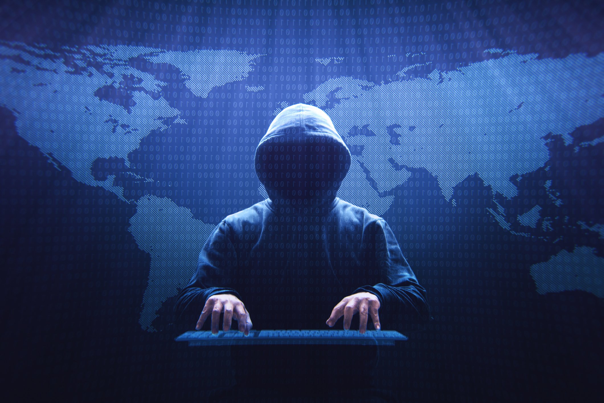 A hacker in a hoodie with a map of the globe behind him. 
