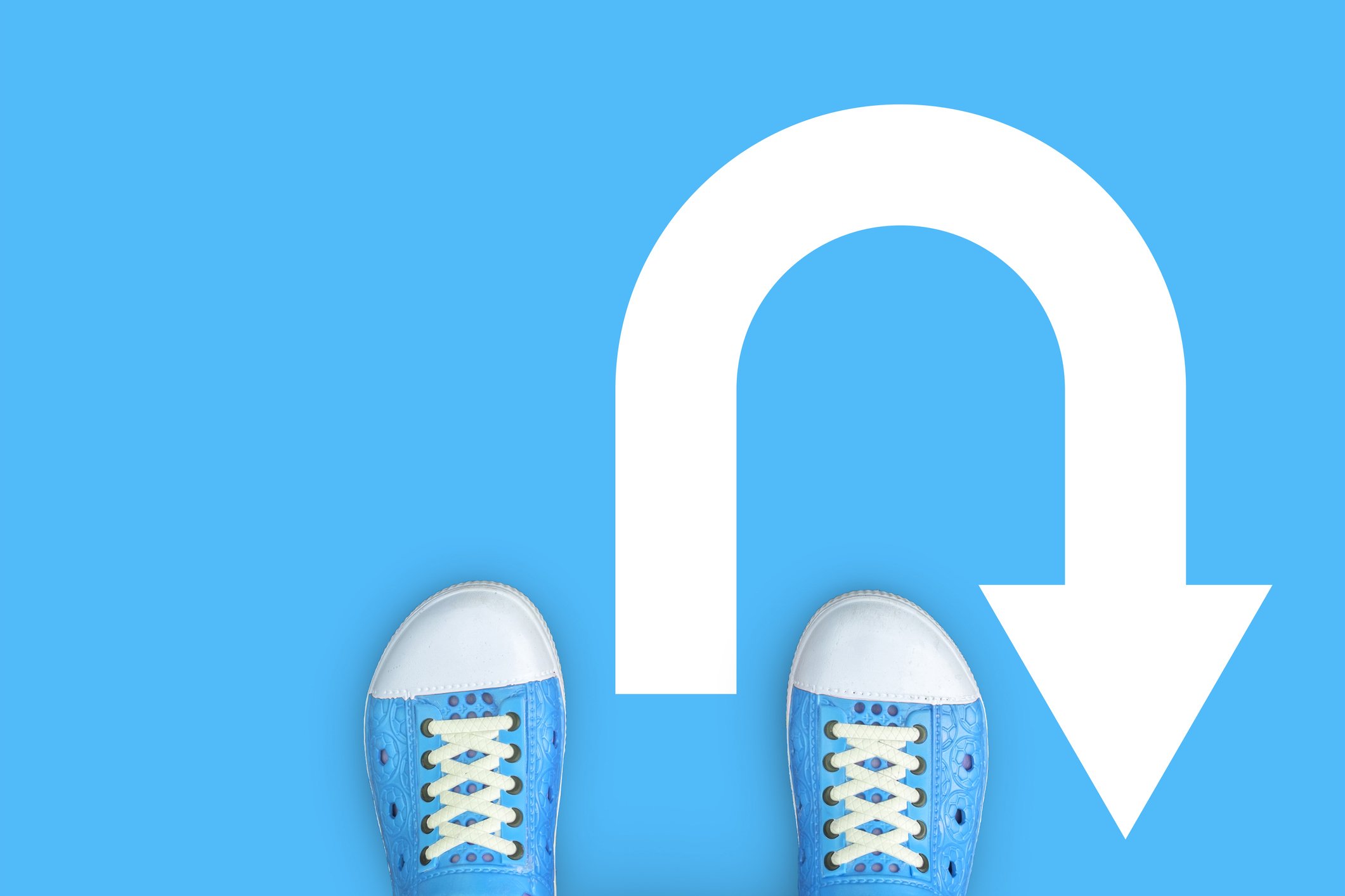 A U-turn sign on a blue floor with the edge of a person's shoes showing.