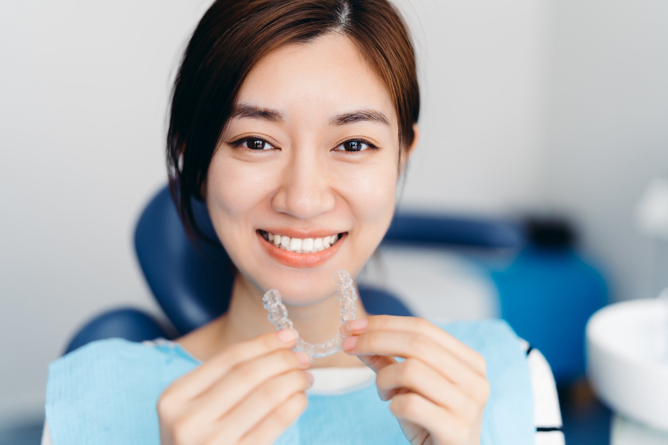 A dental patient holds a clear aligner while sitting in an exam chair.