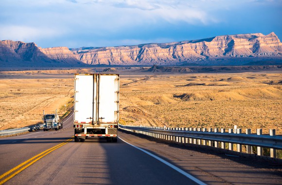 18-wheeler on the highway heading into desert mountains.
