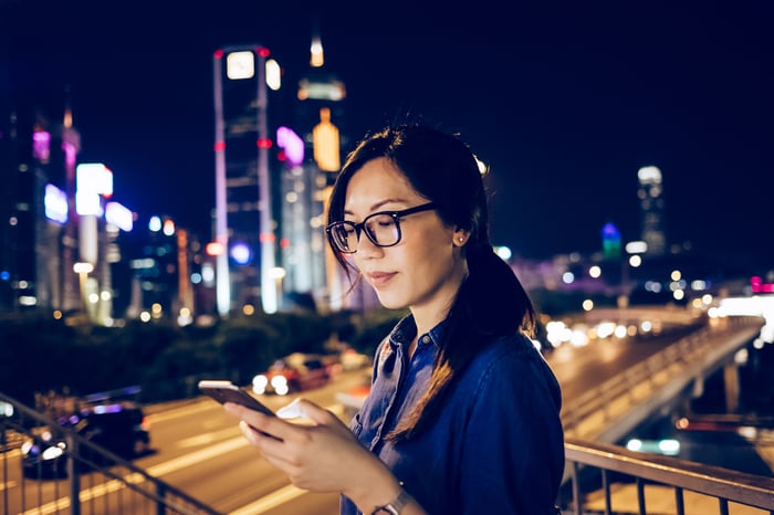 Someone using a smartphone. A city skyline is in the background.