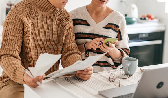 Two people sit at a desk with papers and a calculator doing taxes.