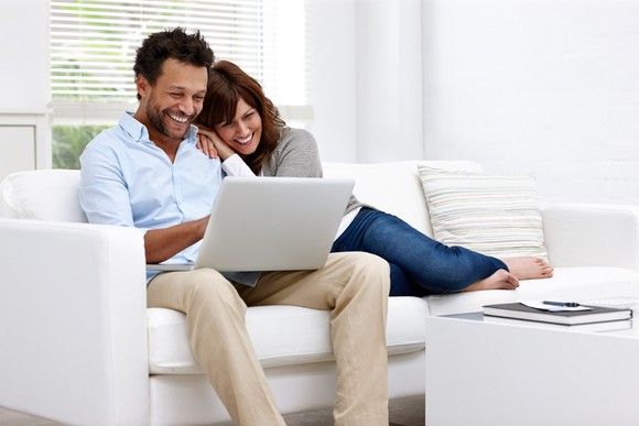 Smiling people on couch looking at a laptop.