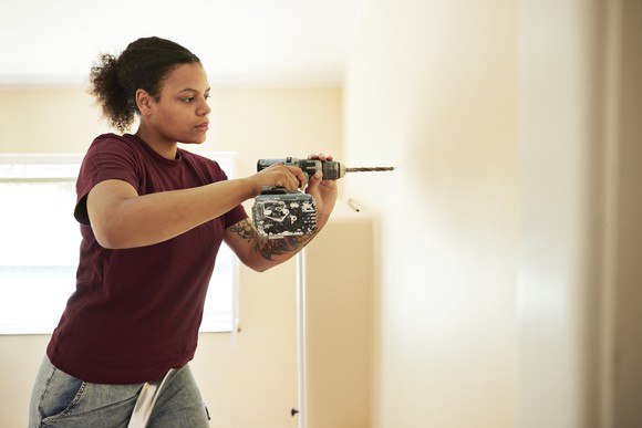 A person drilling into a wall while renovating a room.
