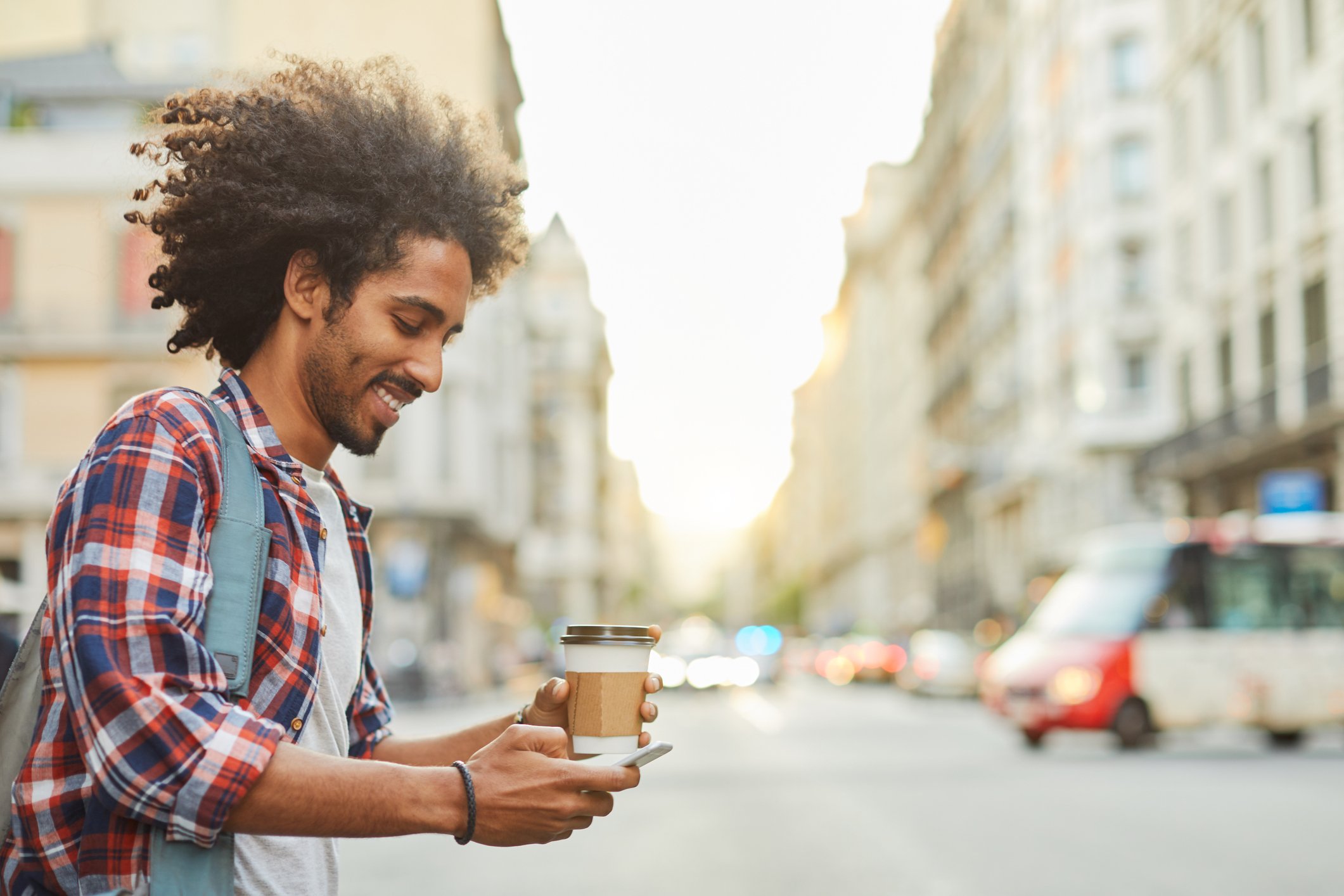 Person looking at phone and holding coffee while crossing city street.